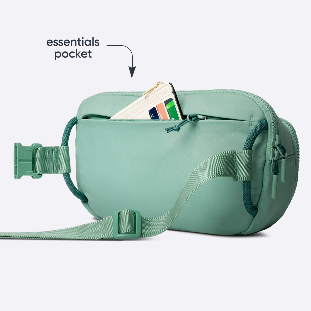 Owala All-Day Crossbody in Sea Glass, sage mint belt bag with matching strap and front zip pocket holding a card, with text reading "essentials pocket" pointing to the open pocket