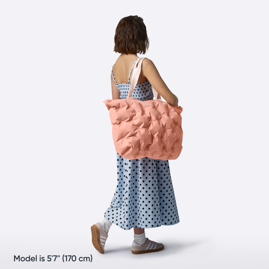 Model walking with the Owala Cloud tote in Rosewood slung over her shoulder, coral pink puffer-quilted body with blush owala-tape handles