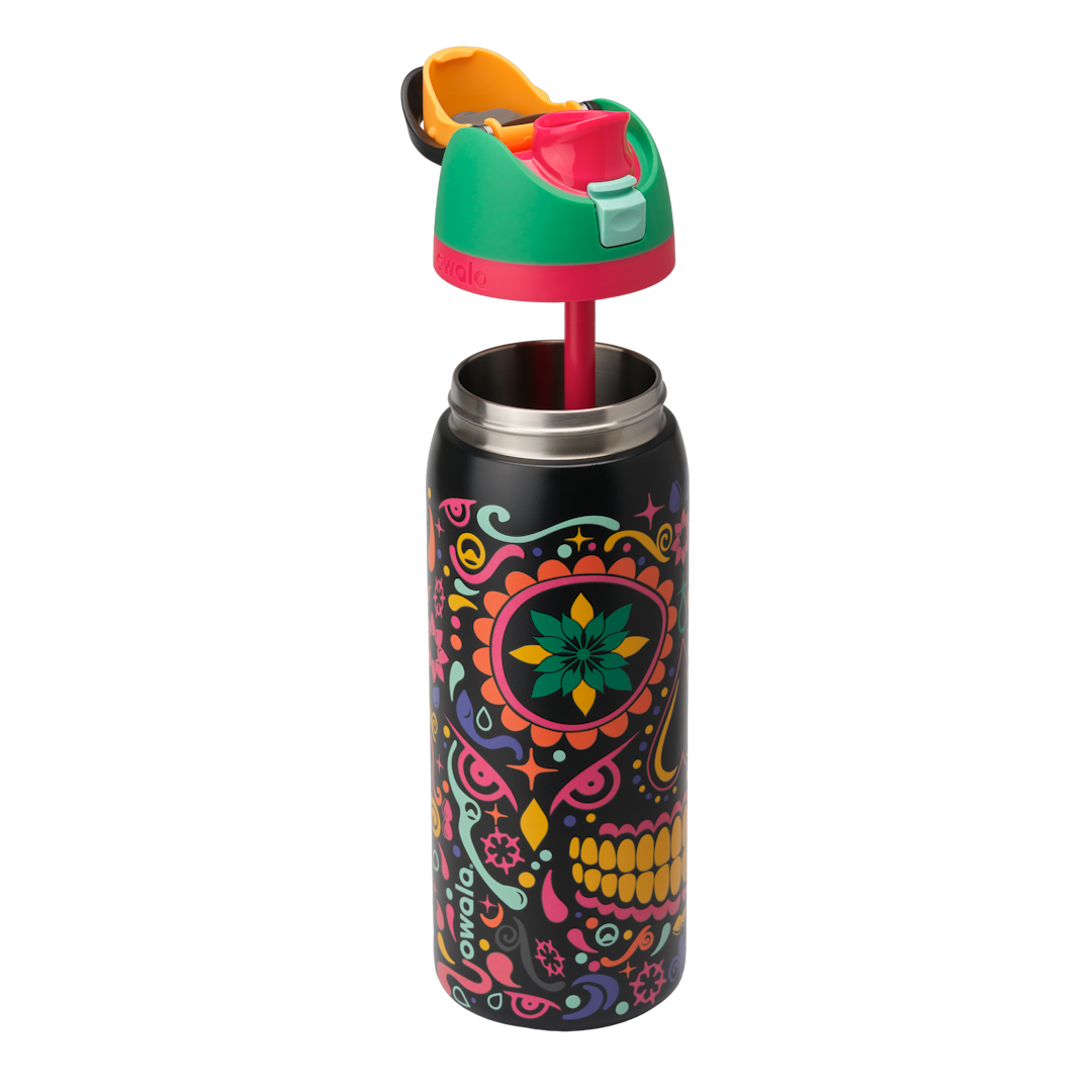 Owala FreeSip Sway 32oz in Sugar Skull, exploded view showing black body with sugar-skull pattern, green flip cap with pink accent ring, orange push-button, and red straw lifted above; glows in the dark