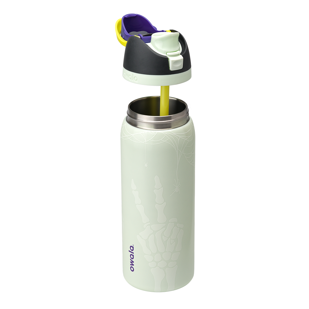 Owala FreeSip 32oz in RIP, pale mint green insulated stainless steel bottle with white skeleton-hand pattern body, dark charcoal lid, yellow carry loop, purple flip cap accent, and pale green accent ring, lid exploded; glows in the dark